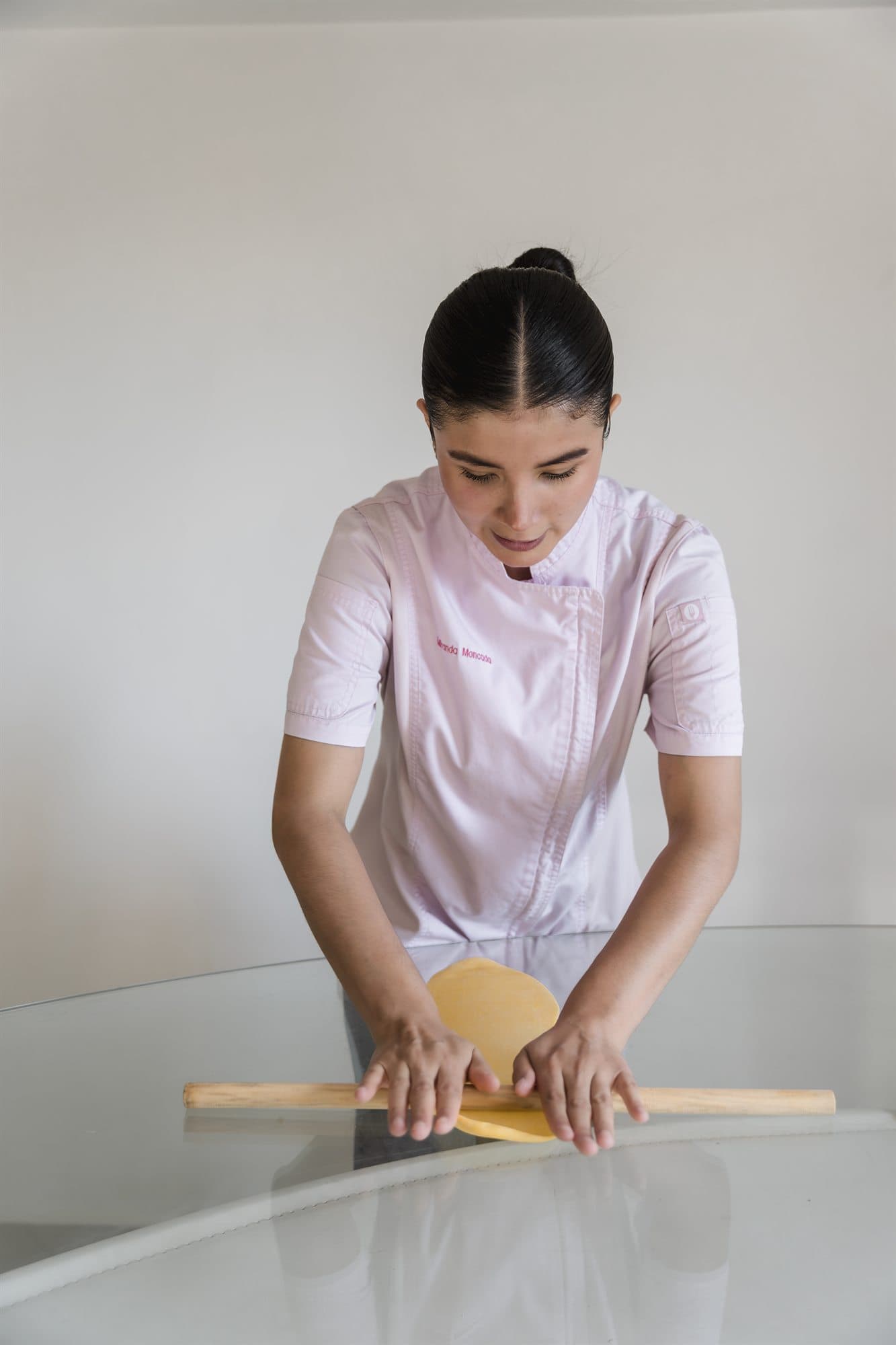 Chef extendiendo una lámina de pasta fresca con rodillo sobre una superficie clara