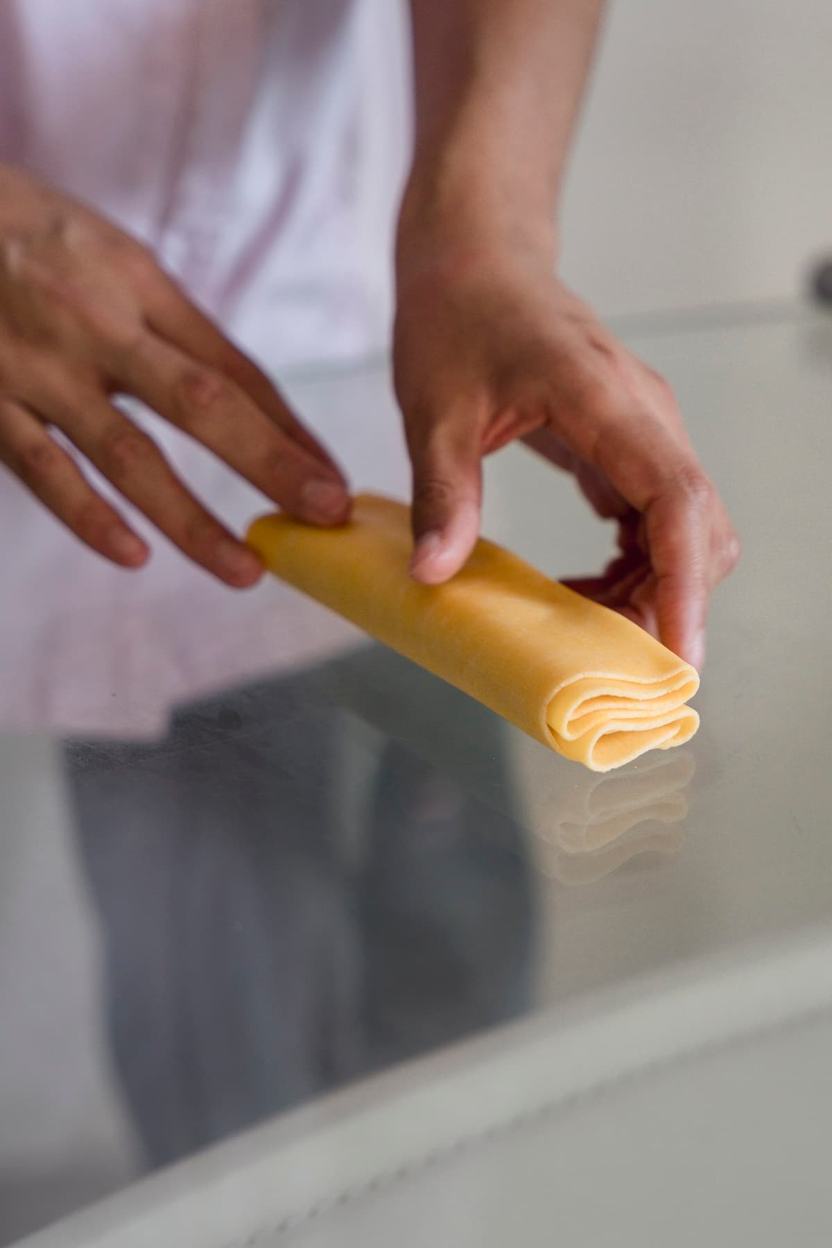 Miranda sosteniendo una lámina de pasta fresca enrollada sobre una mesa de cristal